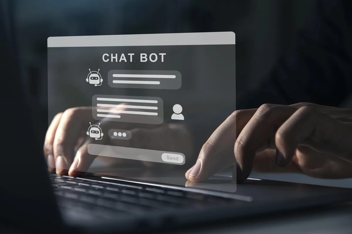Hands typing on a laptop keyboard behind a translucent chat bot window showing a conversation between an AI assistant and a user, with a Send button