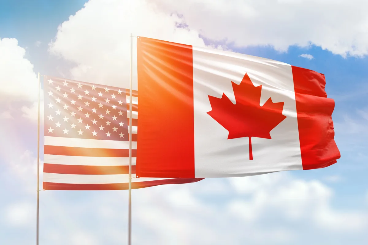 Canadian and American flags flying side by side against a sunny blue sky