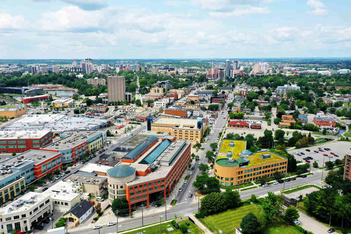 An aerial view of downtown Waterloo, Ontario, with Waterloo City Hall in the foreground and bright shops stretching off into the distance along King Street. The Perimeter Institute can be seen to the left.