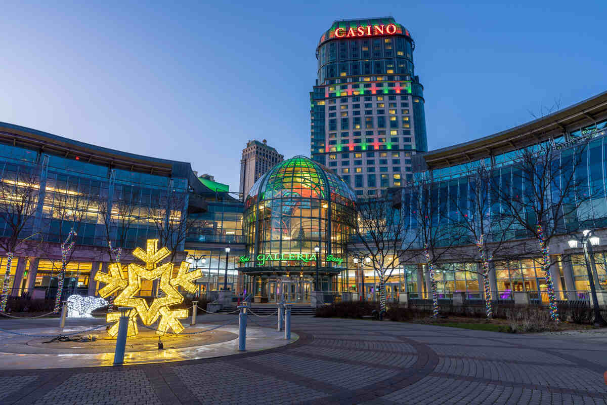 An exterior photo of Fallview Casino in Niagara Falls during the winter. A circular driveway leads up to the main entrance. The building is highlighted in red and green lights for the holidays.