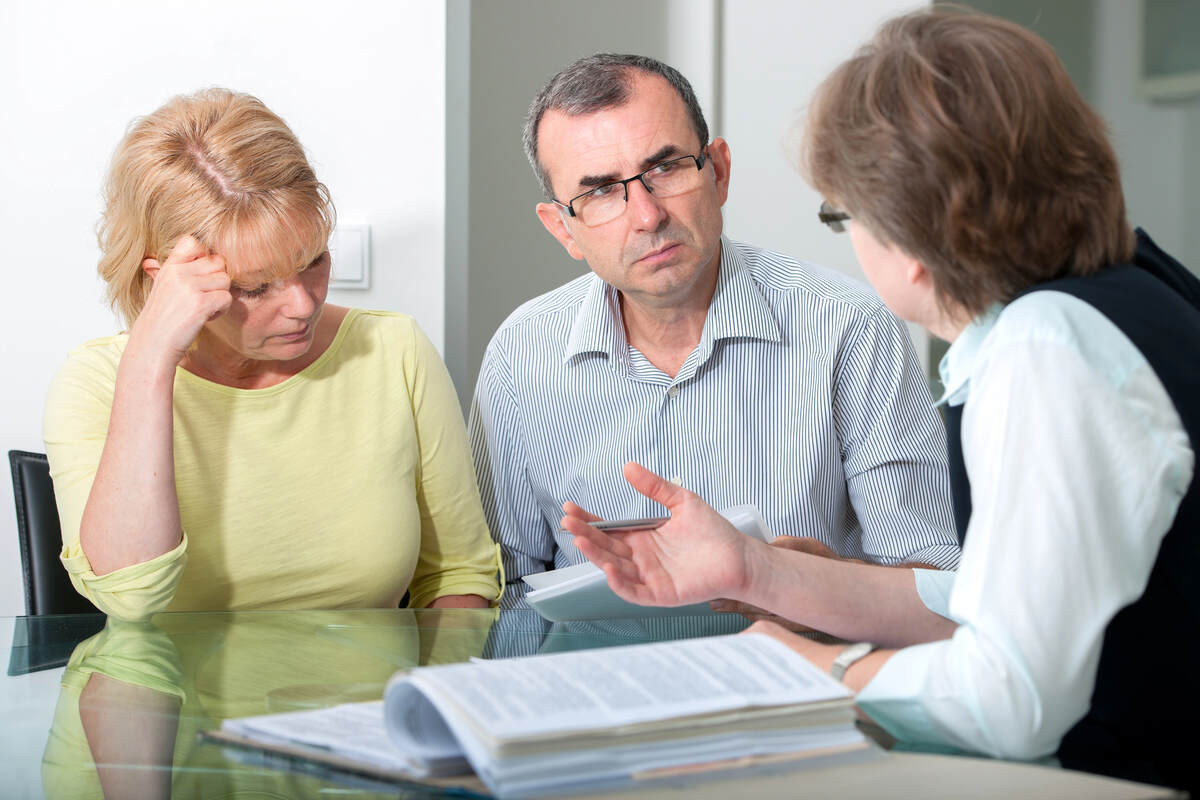 A stressed looking couple reviews paperwork while consulting with a family lawyer.