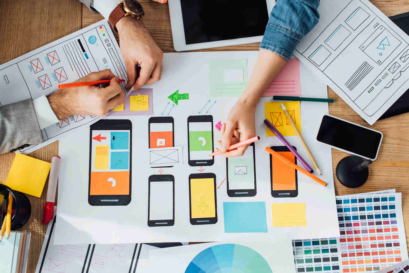 Top-down view of web designers reviewing mobile phone interfaces for website user experience designs