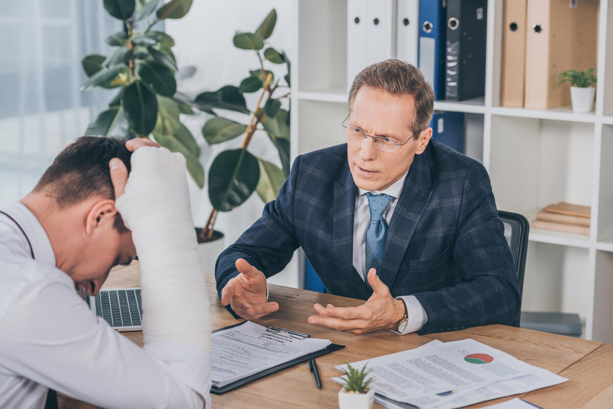 Personal injury lawyer speaking with an injured client wearing a head bandage while reviewing an insurance claim form in an office.