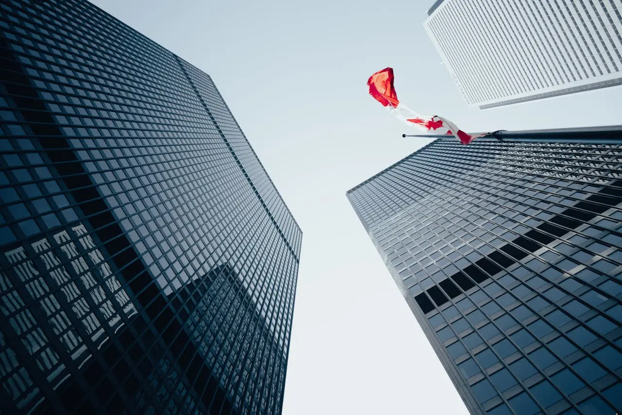 Low angle view of towering skyscrapers and Canadian flag in a modern urban environment.