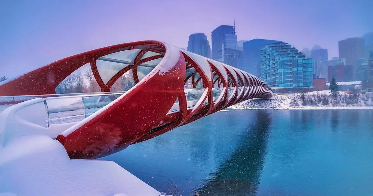 Snow falling on the red Peace Bridge in Calgary, with the downtown skyline behind it