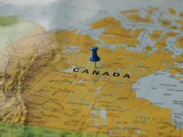 A blue pushpin stuck in the middle of Canada on a map of the world