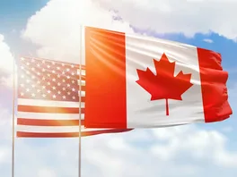 Canadian and American flags flying side by side against a sunny blue sky