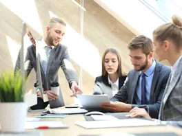 A group of well-dressed young lawyers looking at and discussing various proposals.