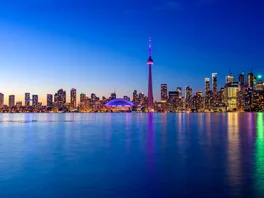 The Toronto skyline at dusk, with the CN Tower lit purple above Lake Ontario