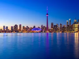 The Toronto skyline at dusk, with the CN Tower lit purple above Lake Ontario